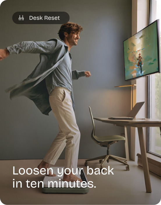 Man leans with his arms spread on the Kiwii Move board beside his desk, steering a game on the TV. Desk Reset: Loosen your back in ten minutes.