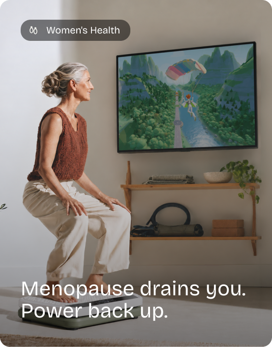 Woman with grey hair squats on the Kiwii Move board while playing a game on the TV. Women's Health: Menopause drains you. Power back up.